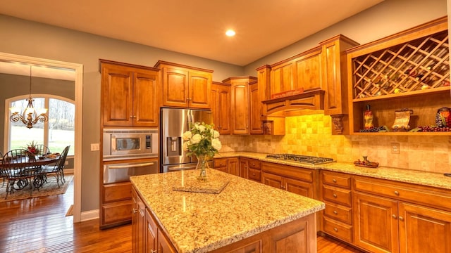 kitchen with a chandelier, hanging light fixtures, appliances with stainless steel finishes, a kitchen island, and light stone countertops