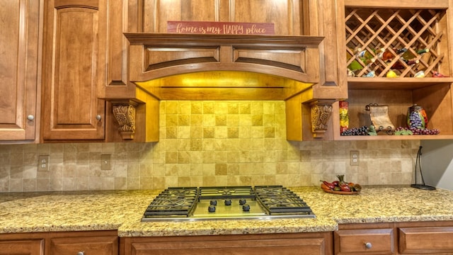 kitchen featuring light stone countertops, stainless steel gas cooktop, custom range hood, and backsplash