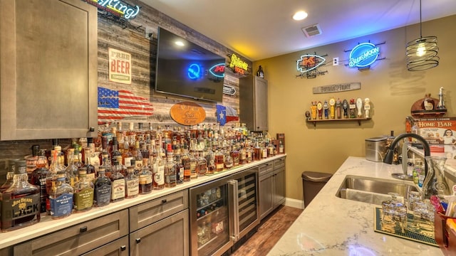 bar with dark wood-type flooring, wine cooler, sink, pendant lighting, and light stone countertops