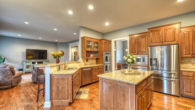 kitchen featuring sink, appliances with stainless steel finishes, a kitchen breakfast bar, light stone countertops, and kitchen peninsula