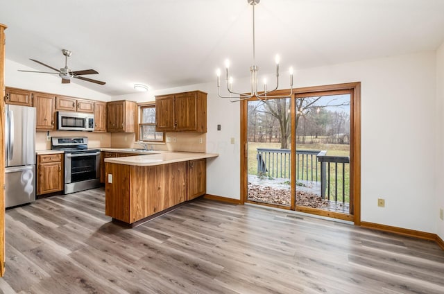 kitchen featuring vaulted ceiling, appliances with stainless steel finishes, pendant lighting, hardwood / wood-style floors, and kitchen peninsula