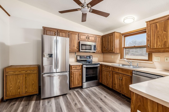 kitchen with vaulted ceiling, sink, light hardwood / wood-style floors, stainless steel appliances, and a textured ceiling