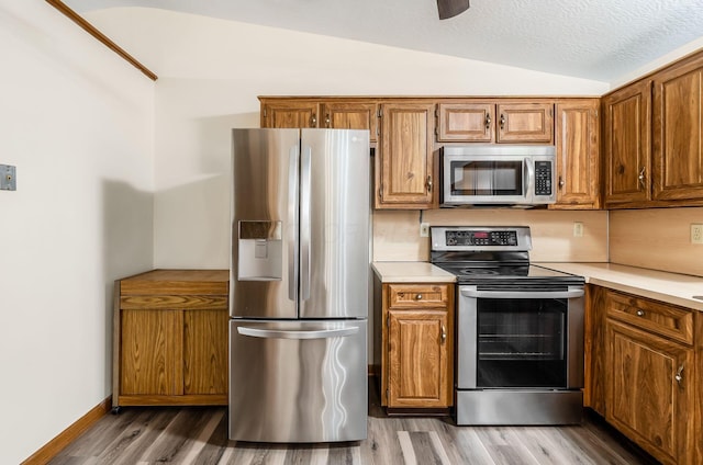 kitchen with vaulted ceiling, light hardwood / wood-style floors, a textured ceiling, and appliances with stainless steel finishes