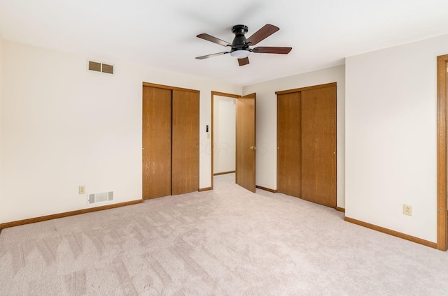 unfurnished bedroom with ceiling fan, light colored carpet, and two closets