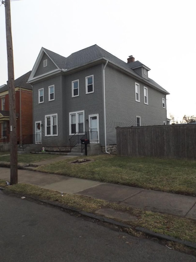 view of front facade featuring a chimney, a front yard, and fence