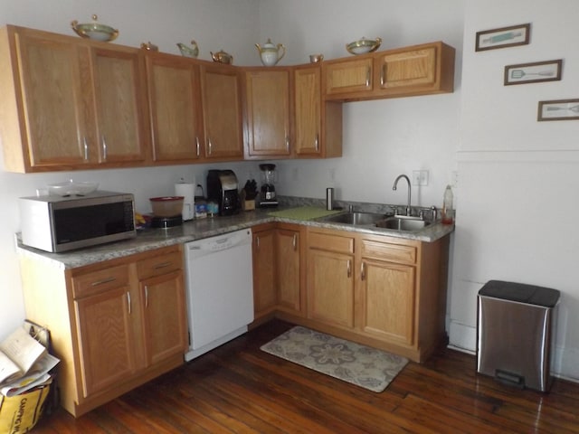 kitchen featuring stainless steel microwave, dark wood-type flooring, light countertops, white dishwasher, and a sink