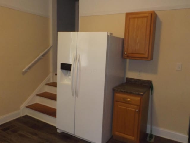 kitchen with dark wood-style floors, brown cabinetry, baseboards, white fridge with ice dispenser, and dark countertops