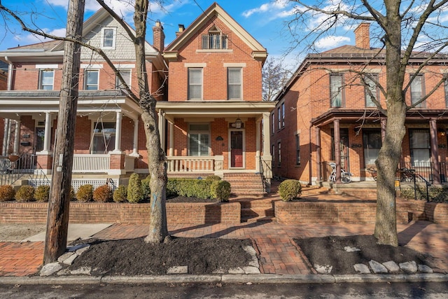 view of front facade with covered porch, a chimney, and brick siding