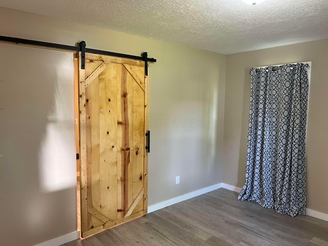 unfurnished bedroom featuring wood-type flooring, a barn door, and a textured ceiling