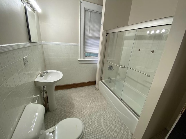 bathroom with enclosed tub / shower combo, toilet, and tile walls