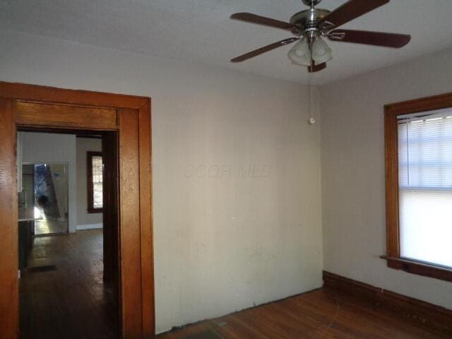 empty room with dark hardwood / wood-style floors, a wealth of natural light, and ceiling fan