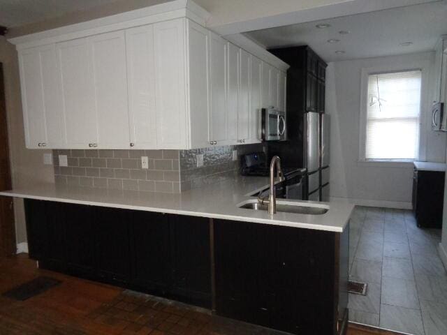 kitchen with decorative backsplash, kitchen peninsula, white cabinets, and appliances with stainless steel finishes