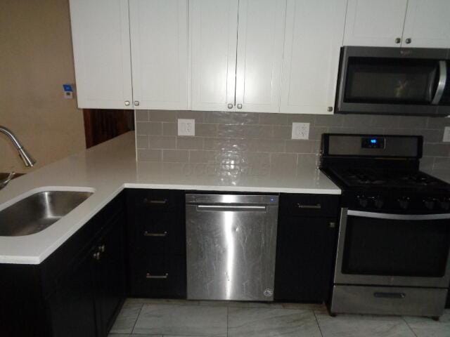 kitchen with stainless steel appliances, white cabinetry, sink, and backsplash