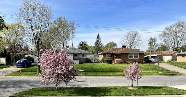 view of front of home featuring driveway, brick siding, a chimney, and a front yard