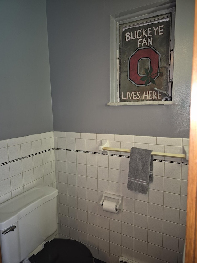 half bathroom featuring wainscoting, toilet, and tile walls