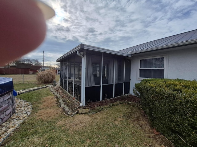 view of property exterior featuring a yard, stucco siding, a sunroom, metal roof, and fence