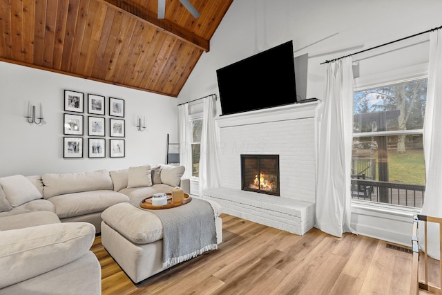 living room with wooden ceiling, light wood-style flooring, a brick fireplace, and a wealth of natural light