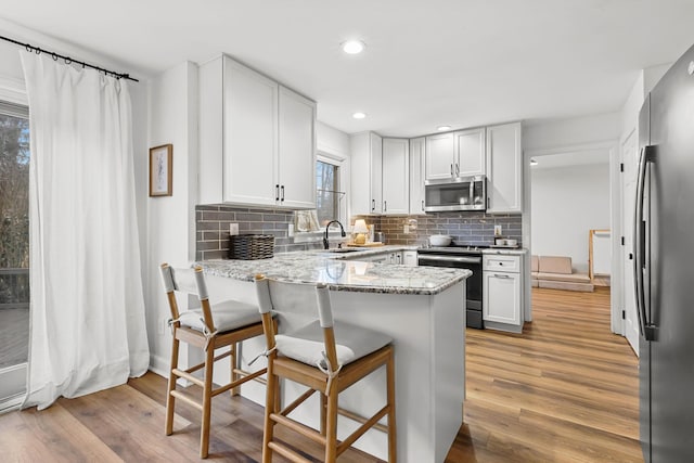 kitchen featuring appliances with stainless steel finishes, a peninsula, light stone countertops, light wood-style floors, and a sink