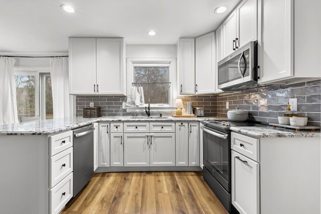 kitchen featuring light stone counters, appliances with stainless steel finishes, light wood-style floors, a sink, and a peninsula