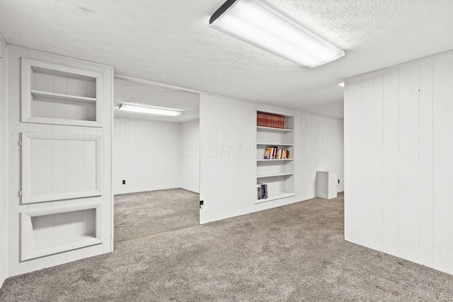 finished basement with built in features, carpet, a textured ceiling, and wooden walls