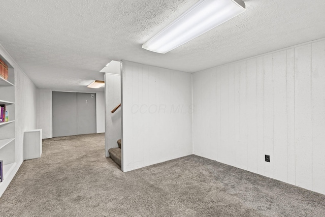 finished basement featuring carpet flooring, a textured ceiling, and stairs