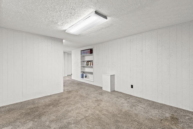 finished below grade area featuring carpet floors, wood walls, a textured ceiling, and built in features