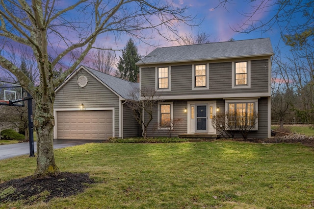 colonial house featuring aphalt driveway, roof with shingles, a yard, and an attached garage