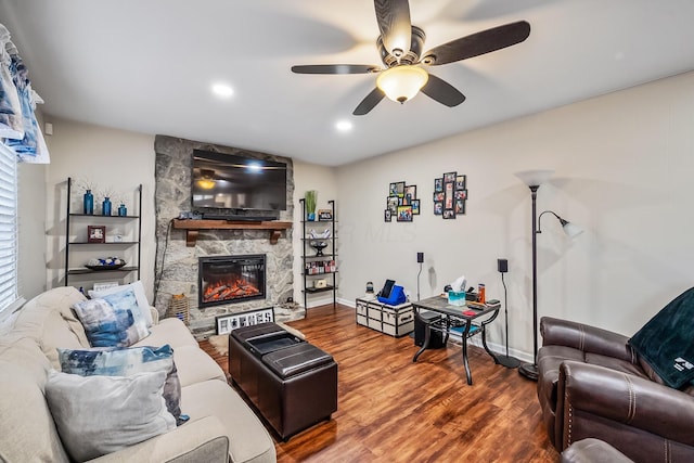 living room featuring hardwood / wood-style flooring, ceiling fan, and a stone fireplace