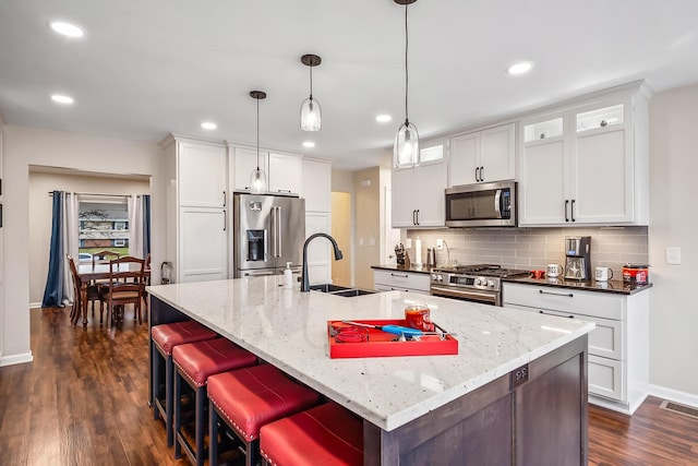 kitchen featuring sink, hanging light fixtures, stainless steel appliances, a kitchen island with sink, and white cabinets