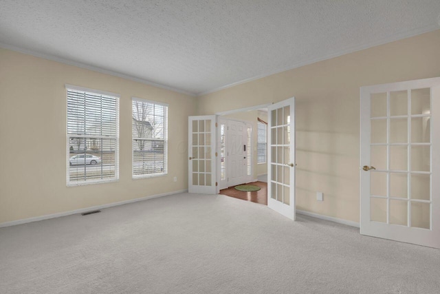 carpeted spare room featuring french doors, crown molding, and a textured ceiling