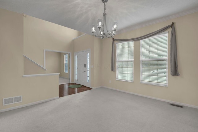 carpeted entrance foyer with crown molding, a textured ceiling, and a chandelier