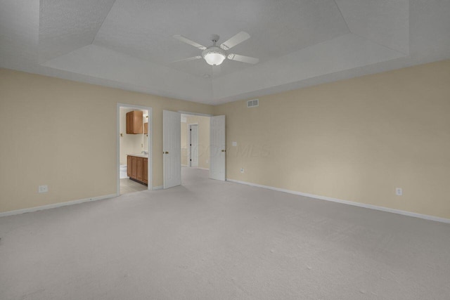 spare room with a textured ceiling, light colored carpet, a raised ceiling, and ceiling fan