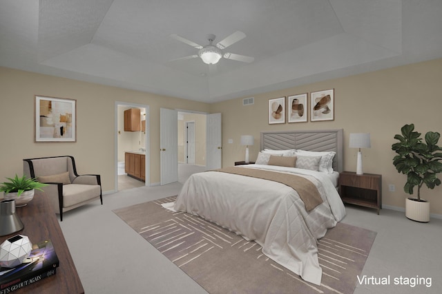 bedroom featuring ceiling fan, ensuite bath, a tray ceiling, and light carpet