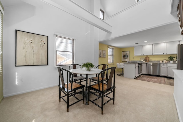 dining space with light carpet, a towering ceiling, and baseboards