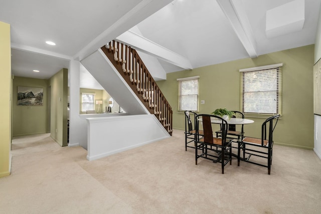 dining area featuring beamed ceiling, a healthy amount of sunlight, stairway, and light colored carpet