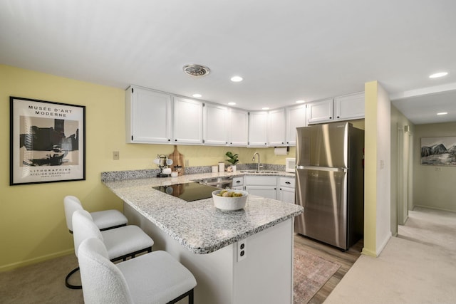 kitchen featuring a peninsula, a breakfast bar area, a sink, and freestanding refrigerator