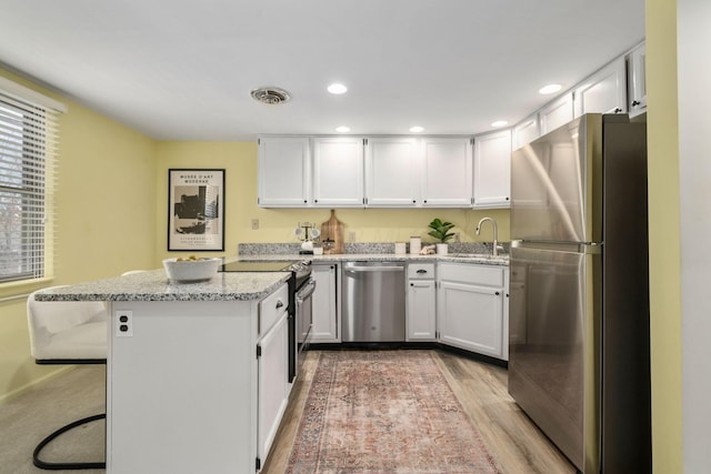 kitchen with stainless steel appliances, visible vents, white cabinets, a sink, and a kitchen bar