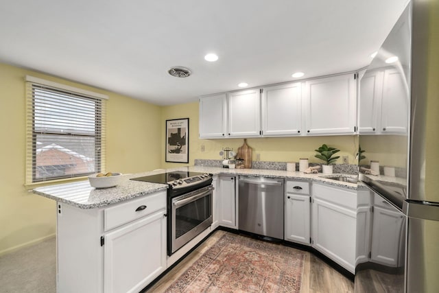 kitchen with visible vents, appliances with stainless steel finishes, a peninsula, light stone countertops, and white cabinetry