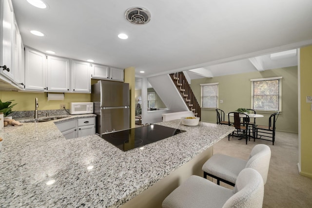 kitchen with white microwave, a peninsula, white cabinetry, freestanding refrigerator, and a kitchen bar