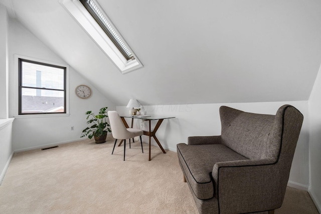 living area featuring light colored carpet, visible vents, vaulted ceiling with skylight, and baseboards