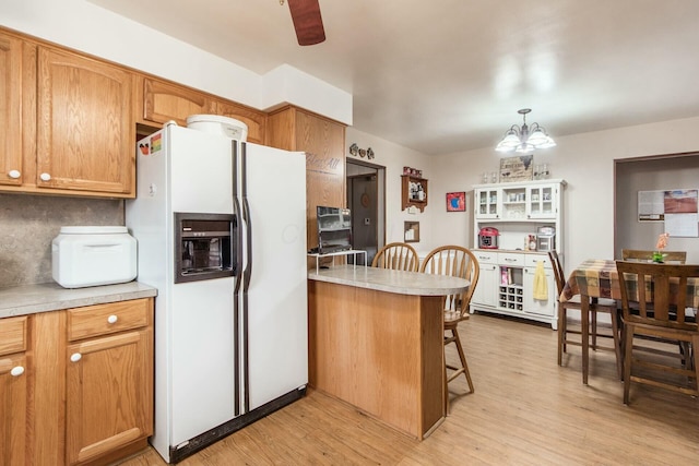 kitchen featuring a breakfast bar, pendant lighting, light wood-type flooring, white fridge with ice dispenser, and an inviting chandelier