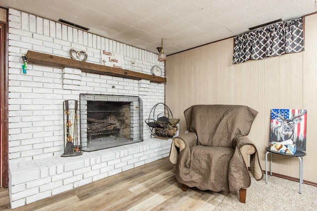 sitting room with hardwood / wood-style flooring, a brick fireplace, and wood walls