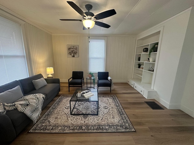 living room with built in features, ceiling fan, wooden walls, dark hardwood / wood-style floors, and ornamental molding