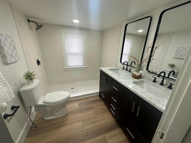 bathroom with wood-type flooring, tiled shower, vanity, and toilet