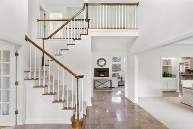 foyer featuring stairway, baseboards, a lit fireplace, and a towering ceiling