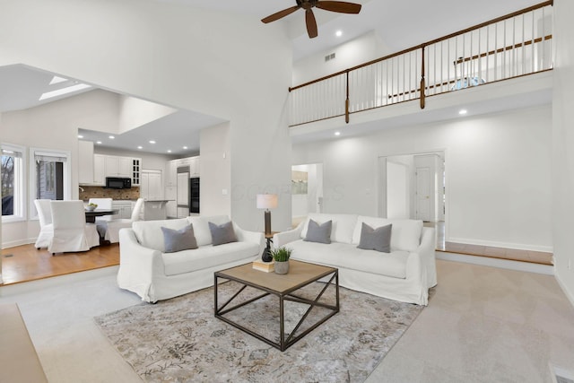 living area featuring visible vents, baseboards, a skylight, a high ceiling, and a ceiling fan