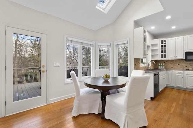 dining area with vaulted ceiling with skylight, light wood-style flooring, recessed lighting, and baseboards