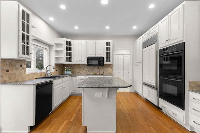 kitchen featuring black appliances, a kitchen island, light wood-style flooring, white cabinetry, and a sink