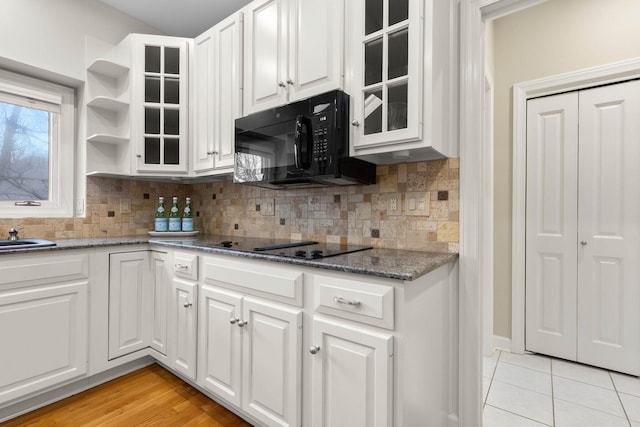 kitchen with black appliances, white cabinets, glass insert cabinets, and tasteful backsplash