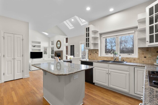 kitchen with a sink, a kitchen island, vaulted ceiling with skylight, black appliances, and open shelves